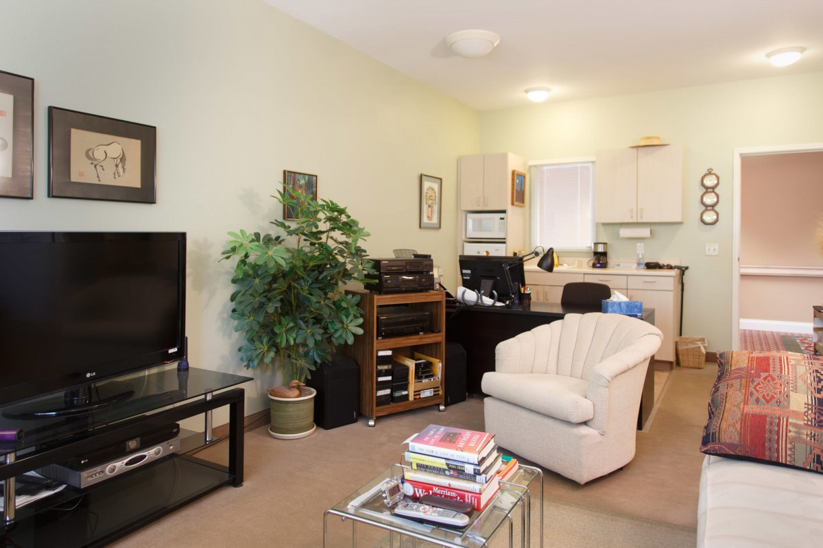 A cozy living room with an armchair, a TV, and a small home office setup.