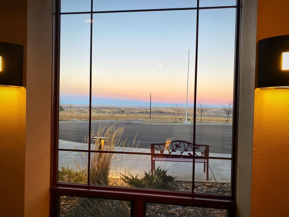 A view of the sunset through a window, featuring a bench and vast landscape.