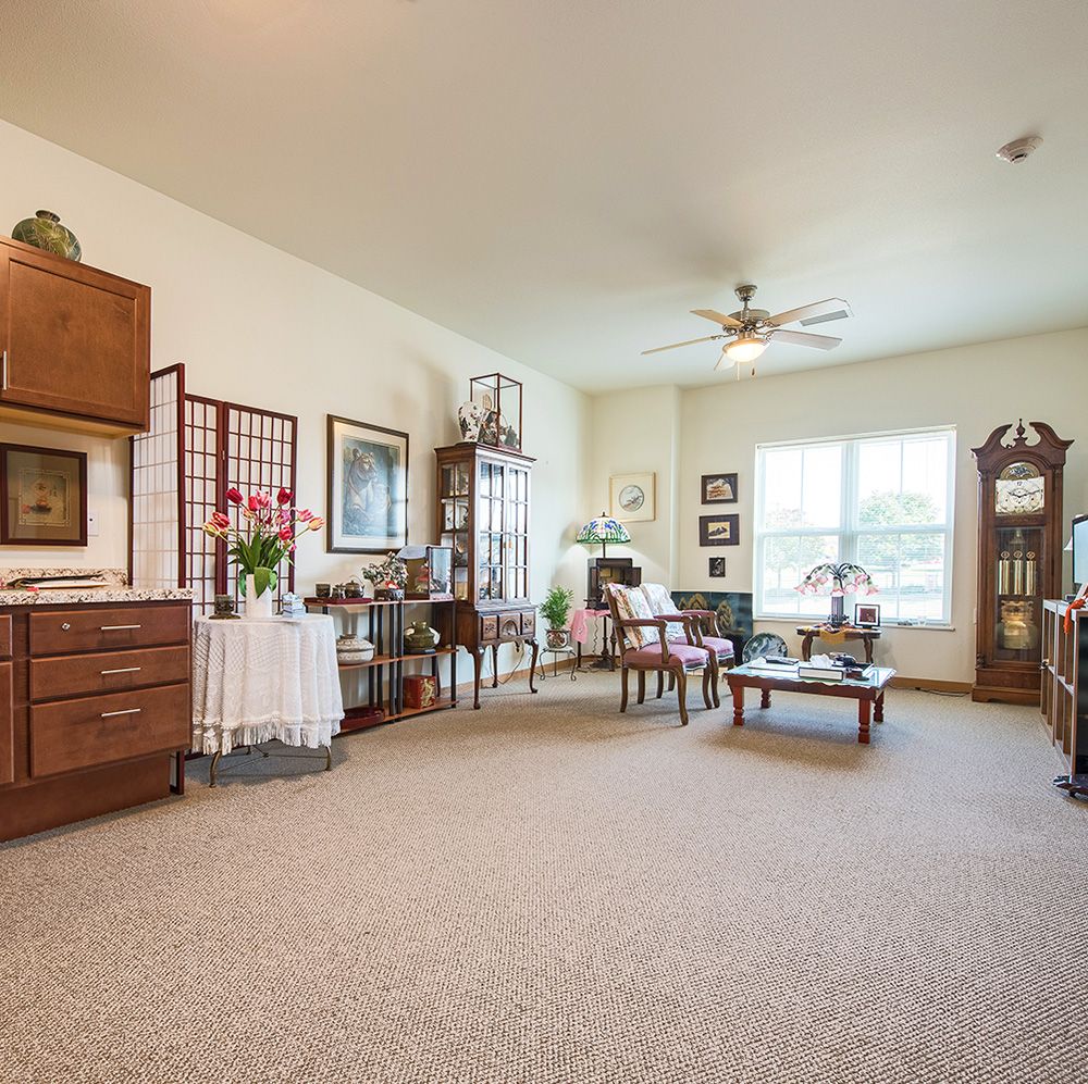 A cozy living room with traditional furniture and a grandfather clock, illuminated by natural light from a large window.