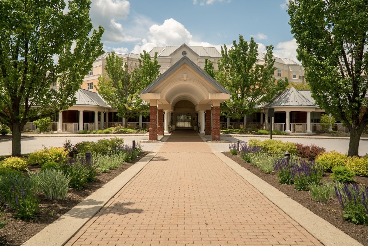 A pathway leads to an elegant building surrounded by landscaped gardens and trees on a sunny day.