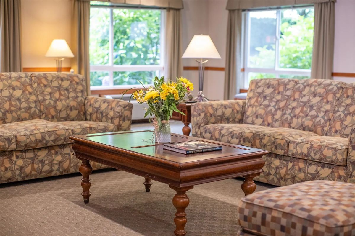 A cozy living room with patterned sofas, a wooden coffee table, and a vase of yellow flowers.