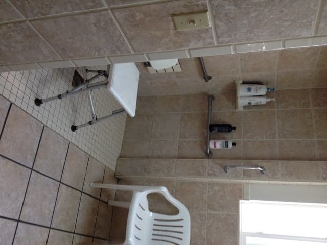 An accessible bathroom with a shower chair and tiled walls.