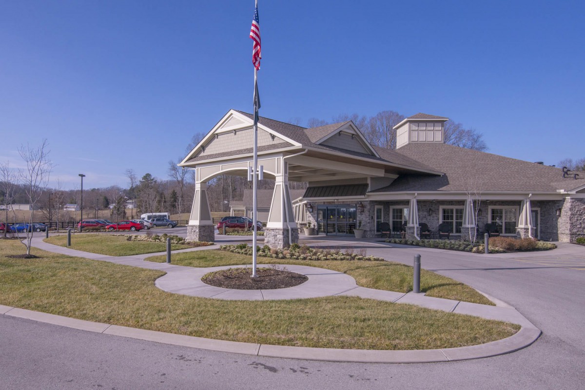 A building with a large entrance and an American flag in front, surrounded by landscaped pathways under a clear blue sky.