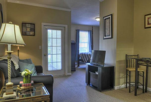 A cozy living room with a television, large windows, and comfortable seating.