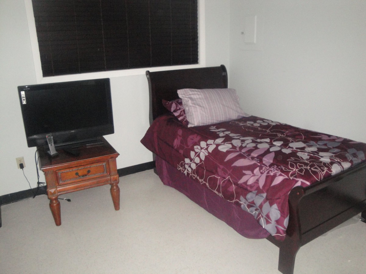 A small bedroom with a single bed and a TV on the nightstand.