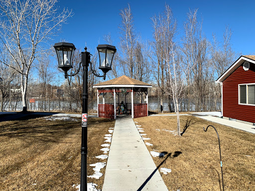 A serene view of a gazebo surrounded by trees, with a clear blue sky and a pathway leading to it.