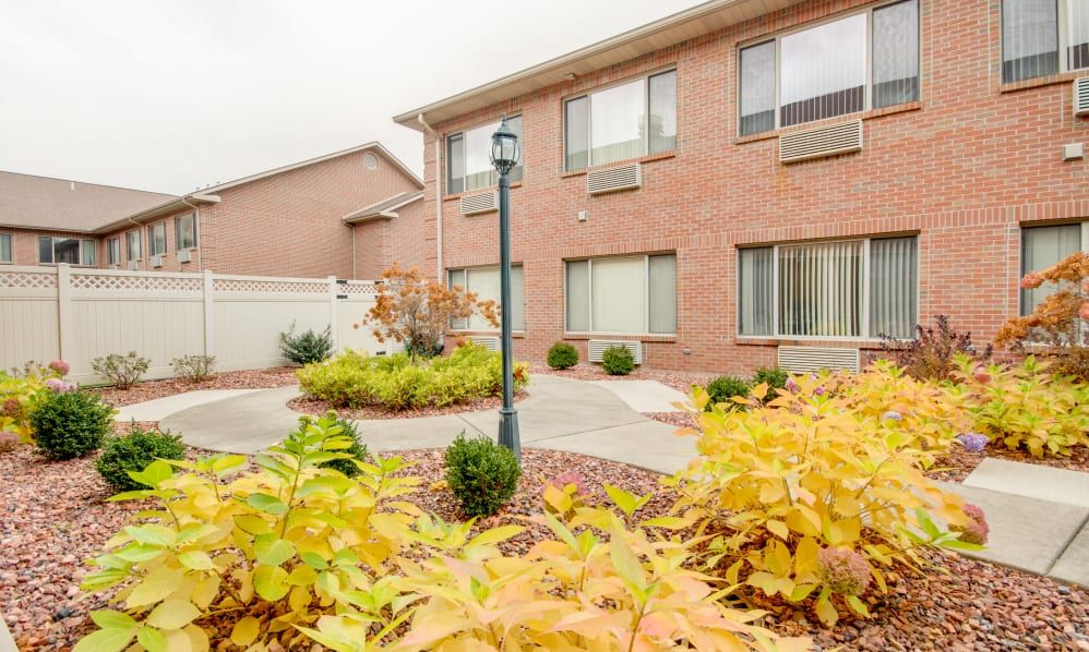 A residential brick building with a landscaped courtyard featuring autumn foliage and a lamp post.