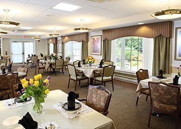 A well-appointed dining room with neatly arranged tables and chairs, featuring large windows and floral decorations.