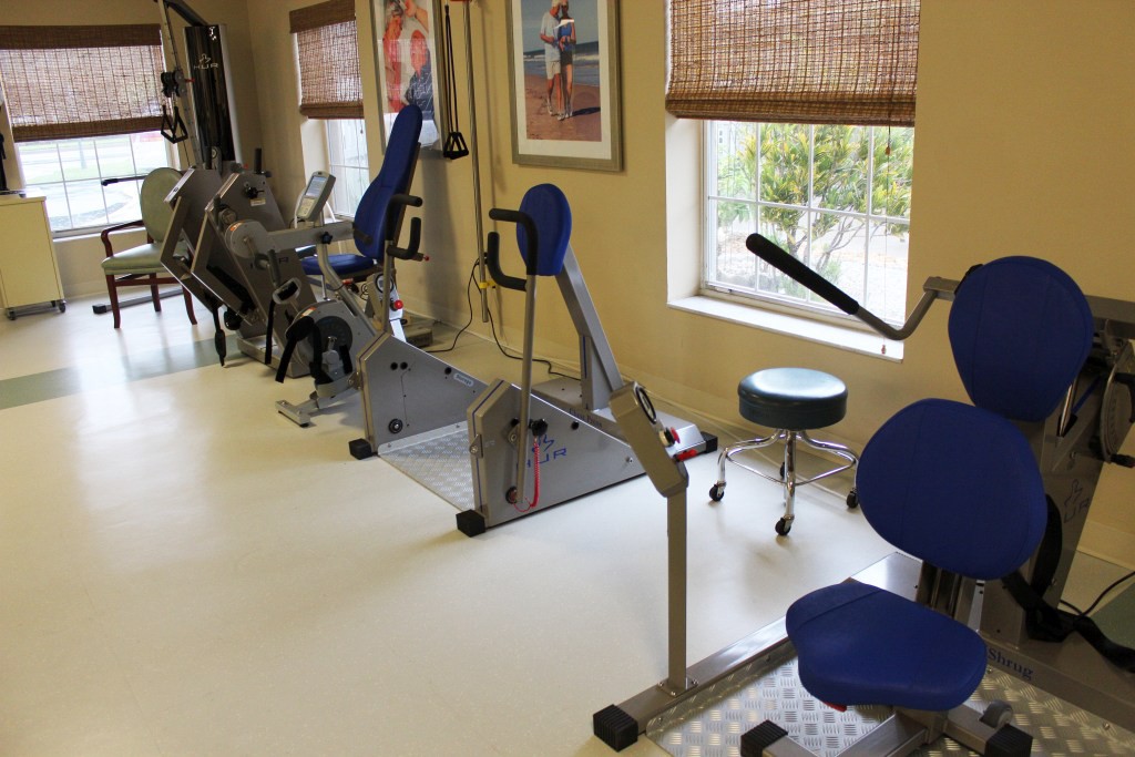 A fitness room with various exercise equipment lined up along the windows.