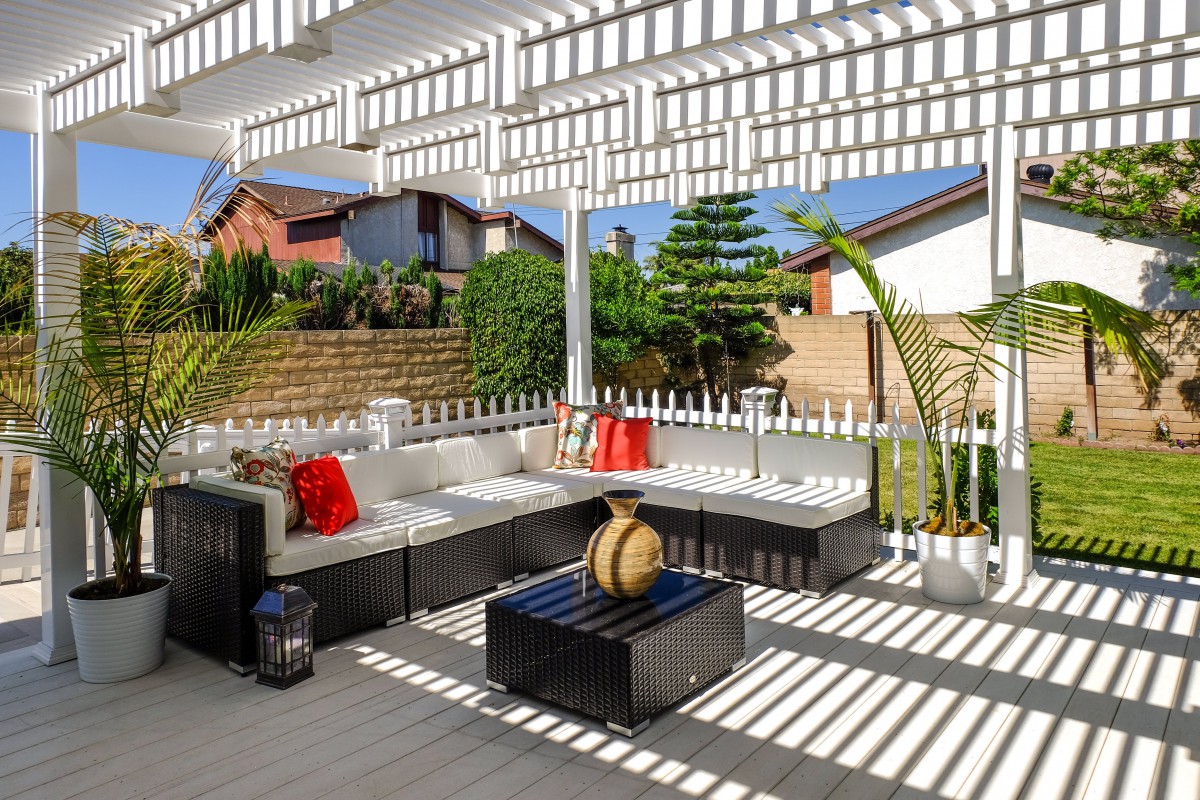A modern outdoor patio with stylish seating under a pergola, featuring decorative pillows and vibrant sunlight.