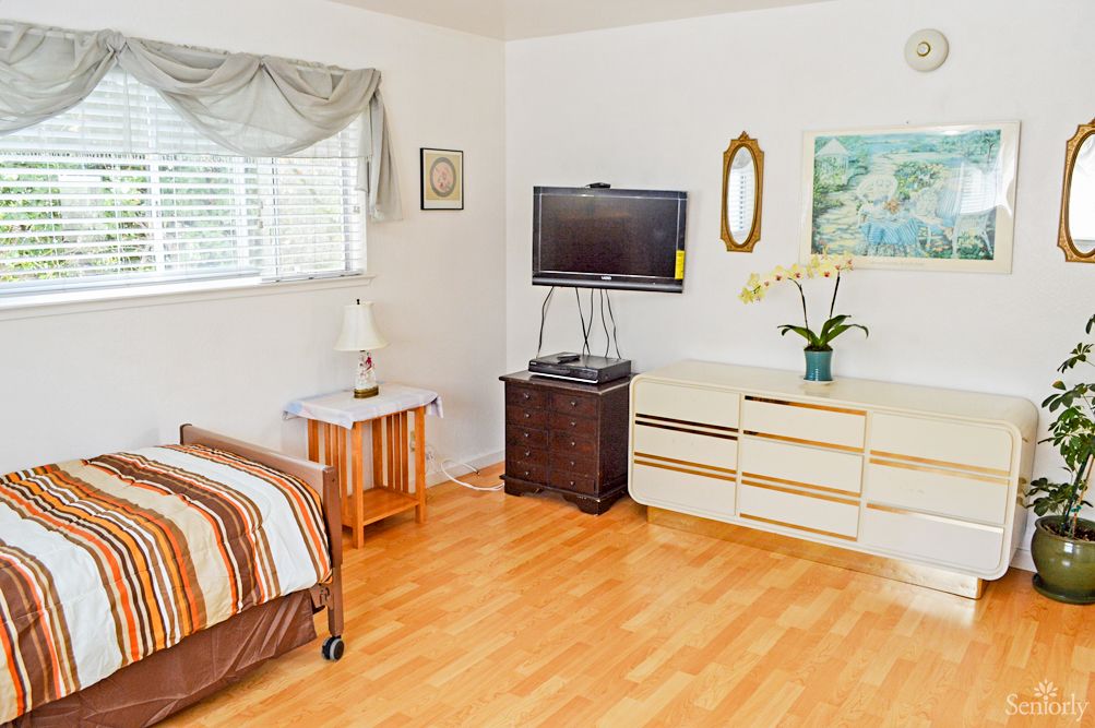 A cozy bedroom featuring a television, dresser, and window with natural light.