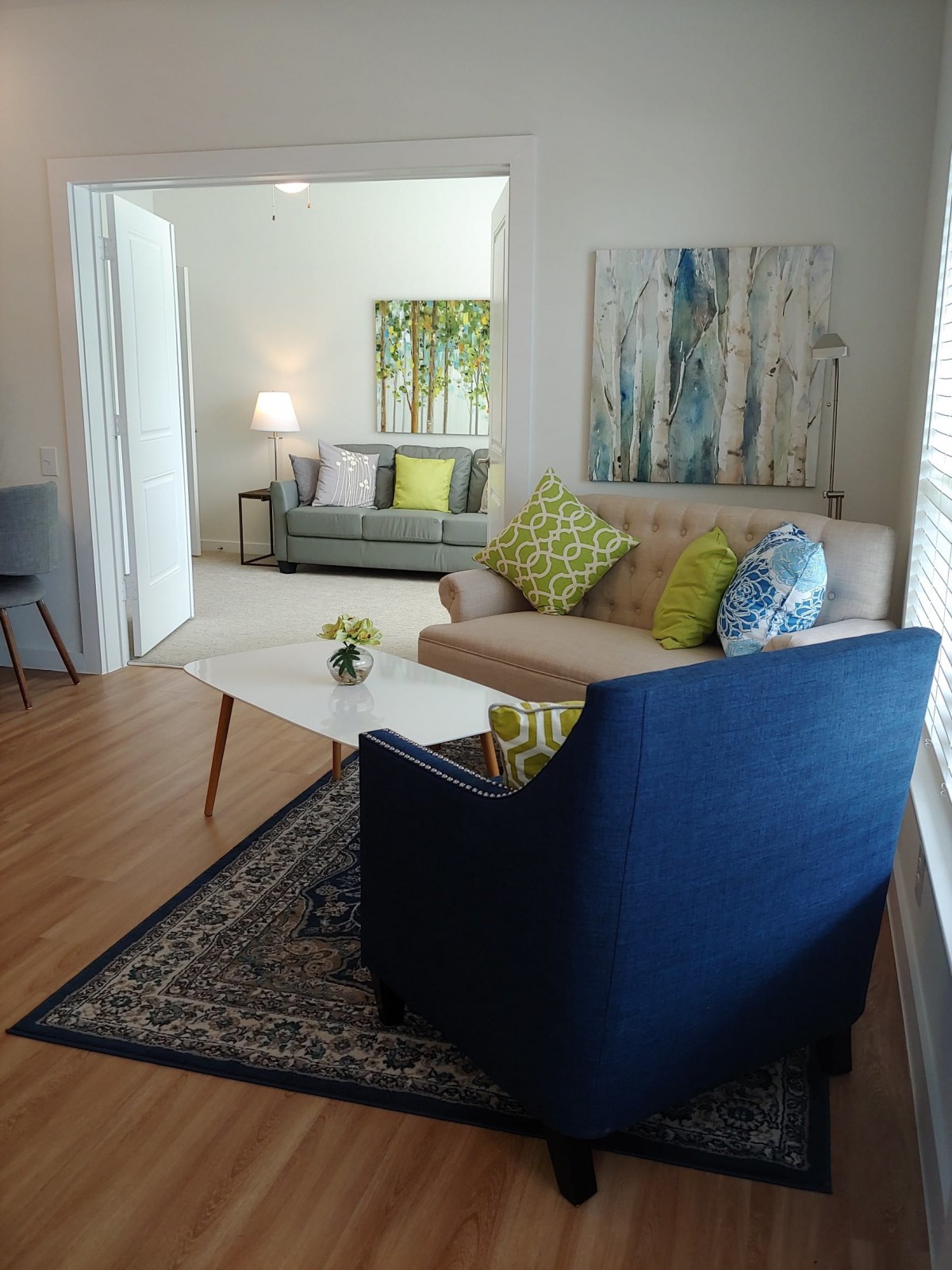 A cozy living room with modern furnishings, including a blue armchair, a beige sofa, and decorative cushions, complemented by abstract artwork and a coffee table.
