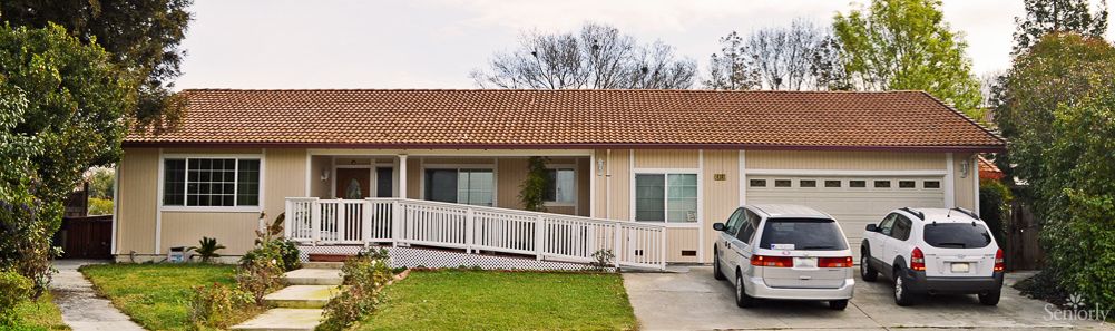 A single-story house with a tiled roof, featuring a ramp leading to the front entrance and a driveway alongside a green lawn.