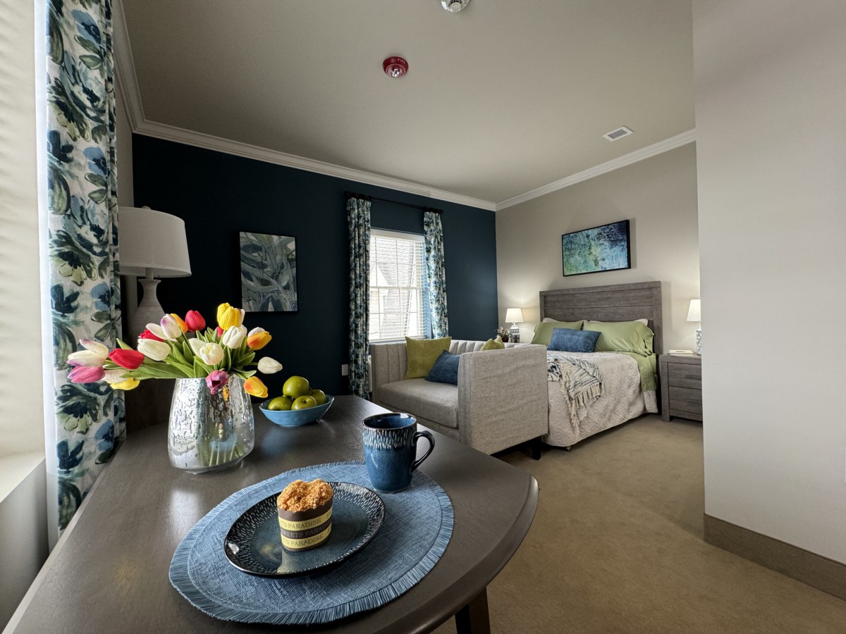 A cozy living space with a sofa, bed, and a table decorated with flowers and a cup.