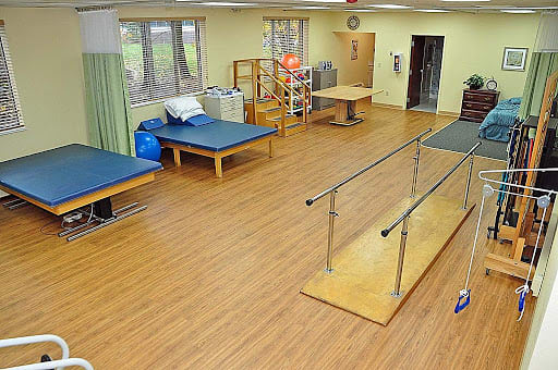 A spacious physical therapy room equipped with parallel bars and exercise tables.