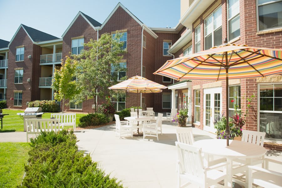 A sunny outdoor patio area with tables, chairs, and umbrellas in front of a building.