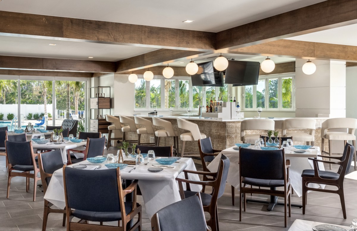 A modern restaurant interior with dining tables and a bar area featuring elegant lighting.