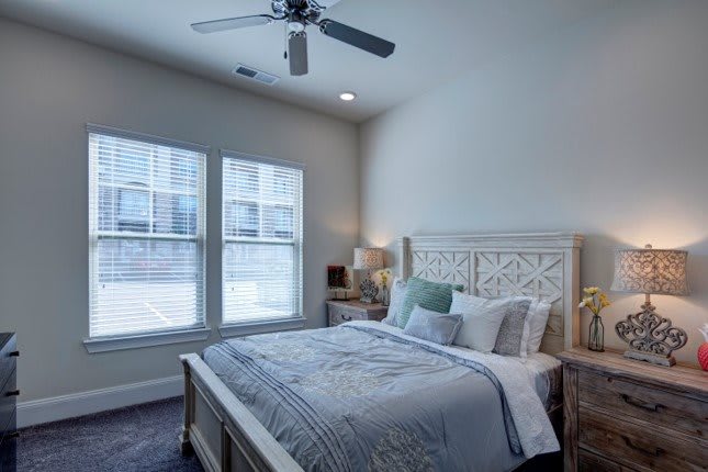 A cozy bedroom with a neatly made bed and a ceiling fan.