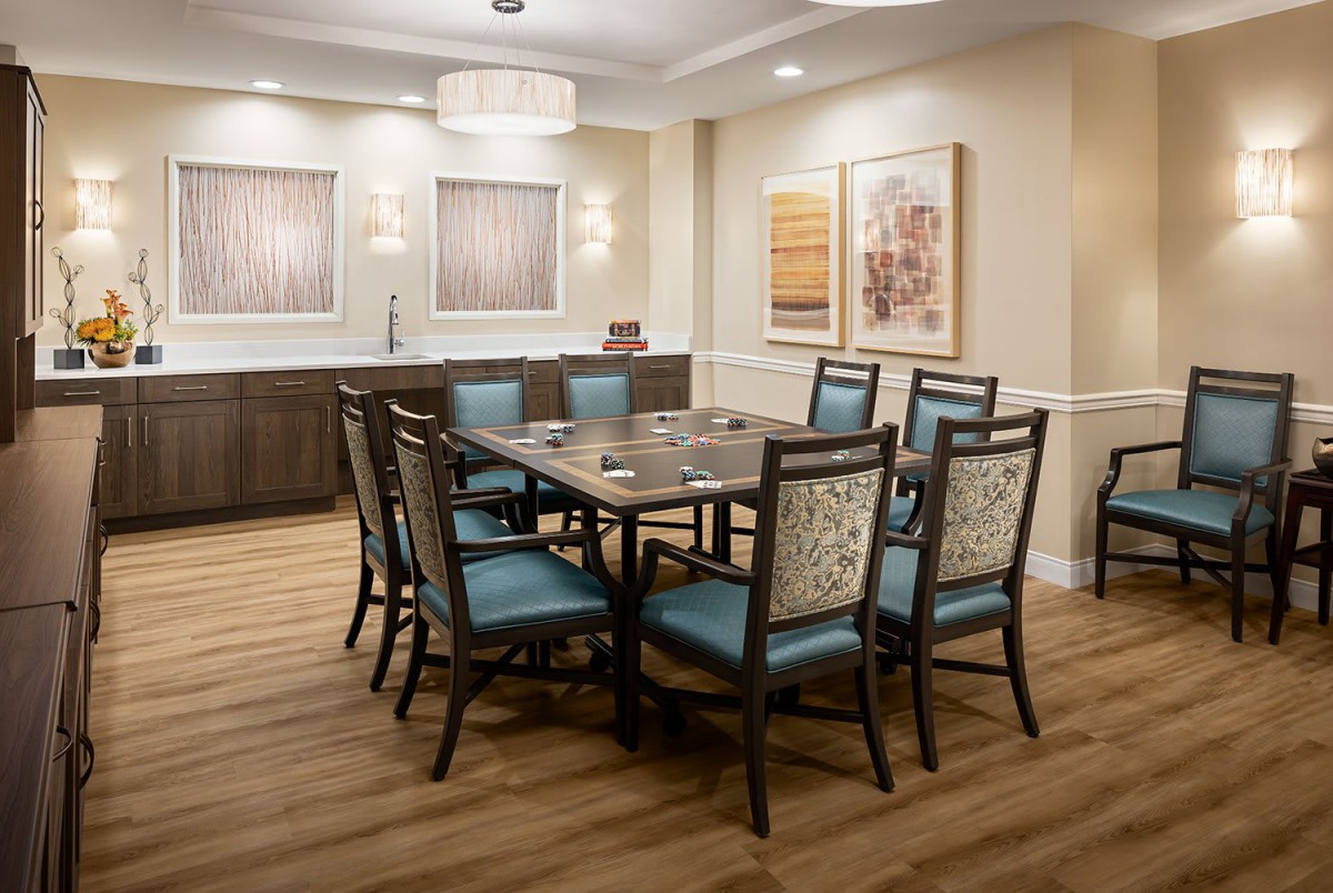 A modern dining room with a rectangular table and six upholstered chairs, featuring wall art and ambient lighting.