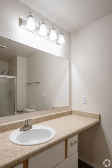 A minimalist bathroom featuring a countertop with a sink, a large mirror, and a shower area.