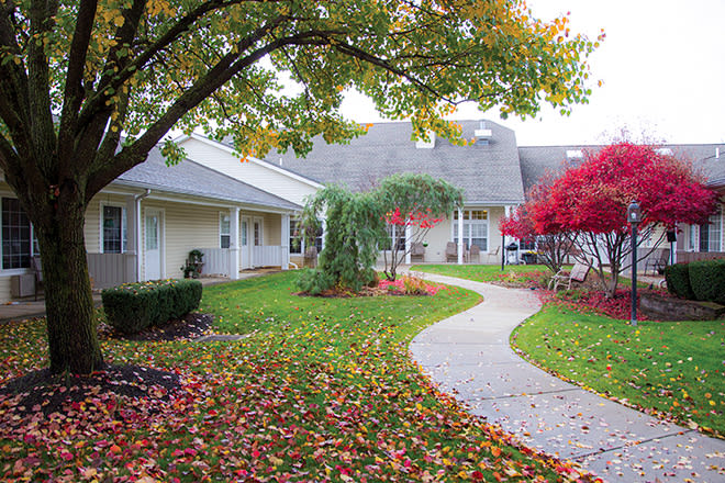 A serene autumn scene with a winding pathway through colorful foliage and adjacent buildings.