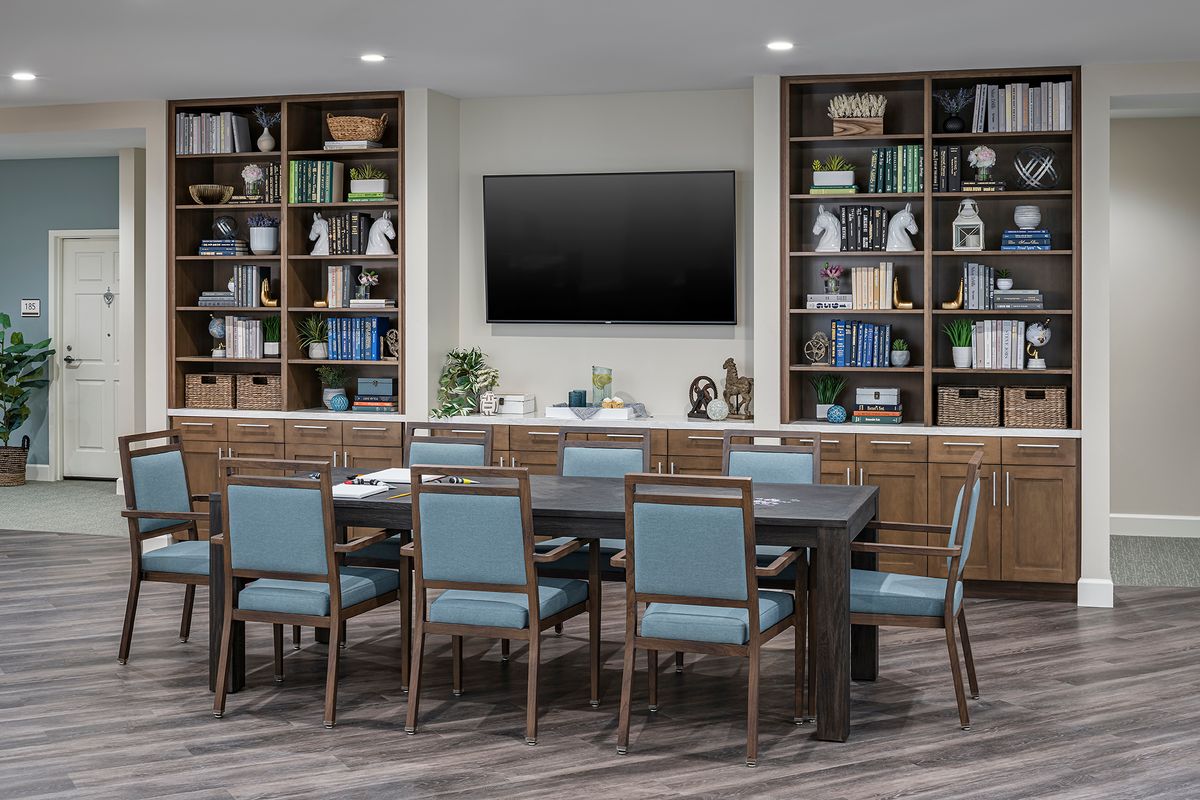 A modern conference room with a large table, chairs, and bookshelves.