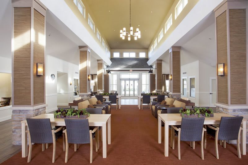 A spacious and modern dining area with high ceilings, featuring multiple tables and chairs under elegant chandeliers.