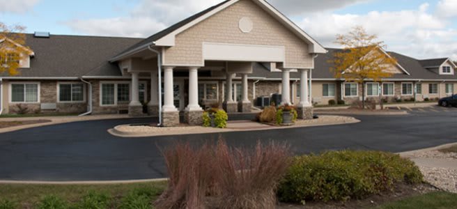 A single-story building with prominent columns at the entrance, surrounded by neatly maintained landscaping and a paved parking area under a cloudy sky.
