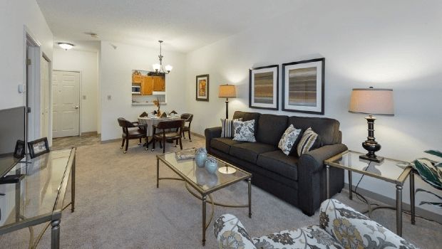 A cozy living room with a dark sofa, glass coffee table, and dining area in the background.