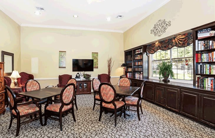 A well-furnished room with tables, chairs, a television, and a bookshelf.