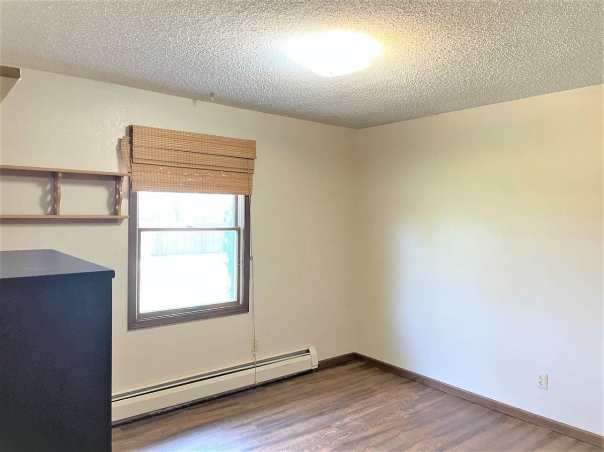 An empty room with wooden floors and a window with blinds.