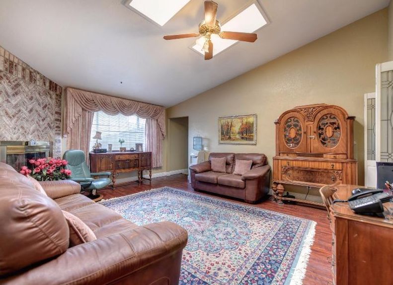 A cozy living room with leather sofas, a colorful area rug, and wooden furniture under a ceiling fan.
