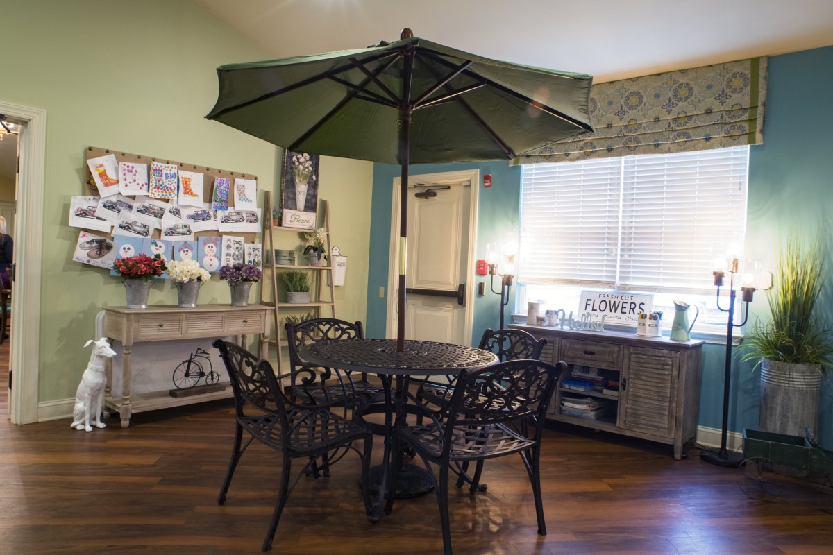 A cozy indoor setting featuring a table with chairs and an umbrella, surrounded by decor.