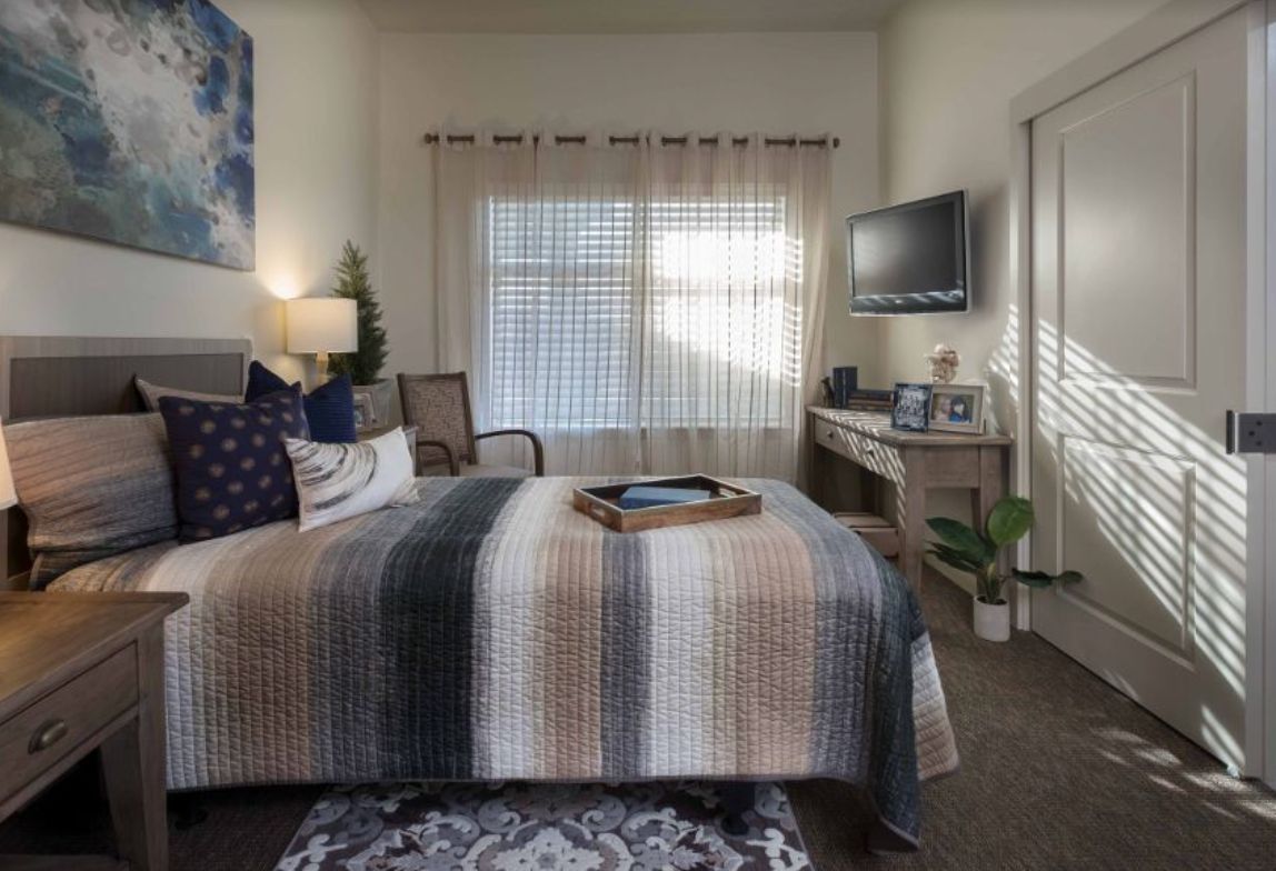 A cozy bedroom with a neatly made bed, television, and warm lighting.