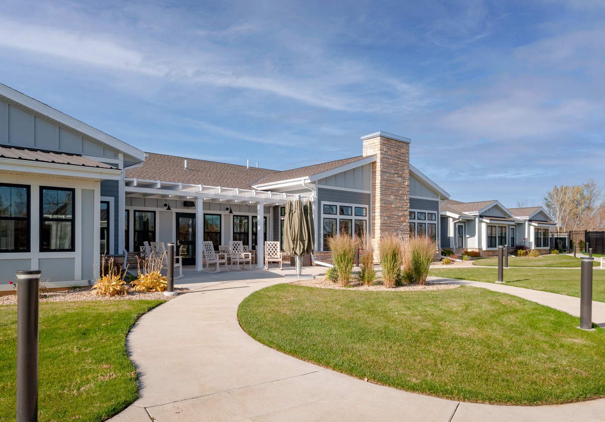 A modern residential building with a landscaped lawn and walkway, set under a clear blue sky.