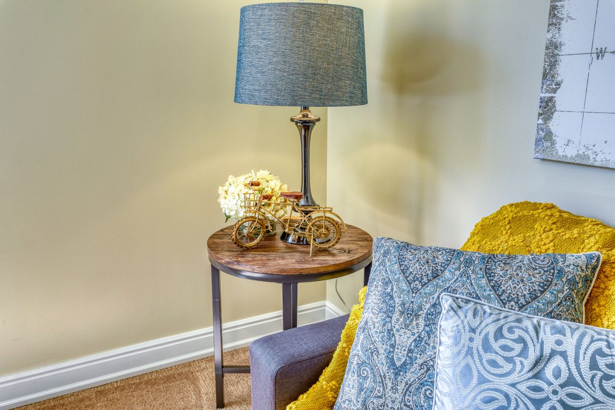 A cozy nook featuring a side table with a lamp, decorative flowers, and comfortable cushions.