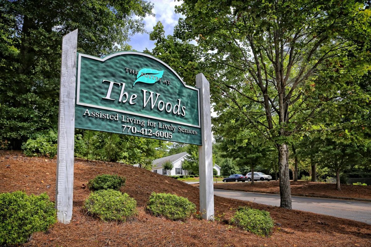 Entrance sign to The Woods community, surrounded by greenery and well-maintained landscaping.