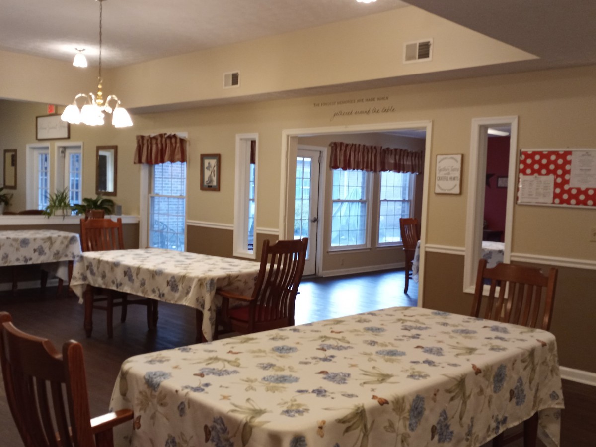 A cozy dining area with tables covered in floral-patterned tablecloths and surrounded by wooden chairs.