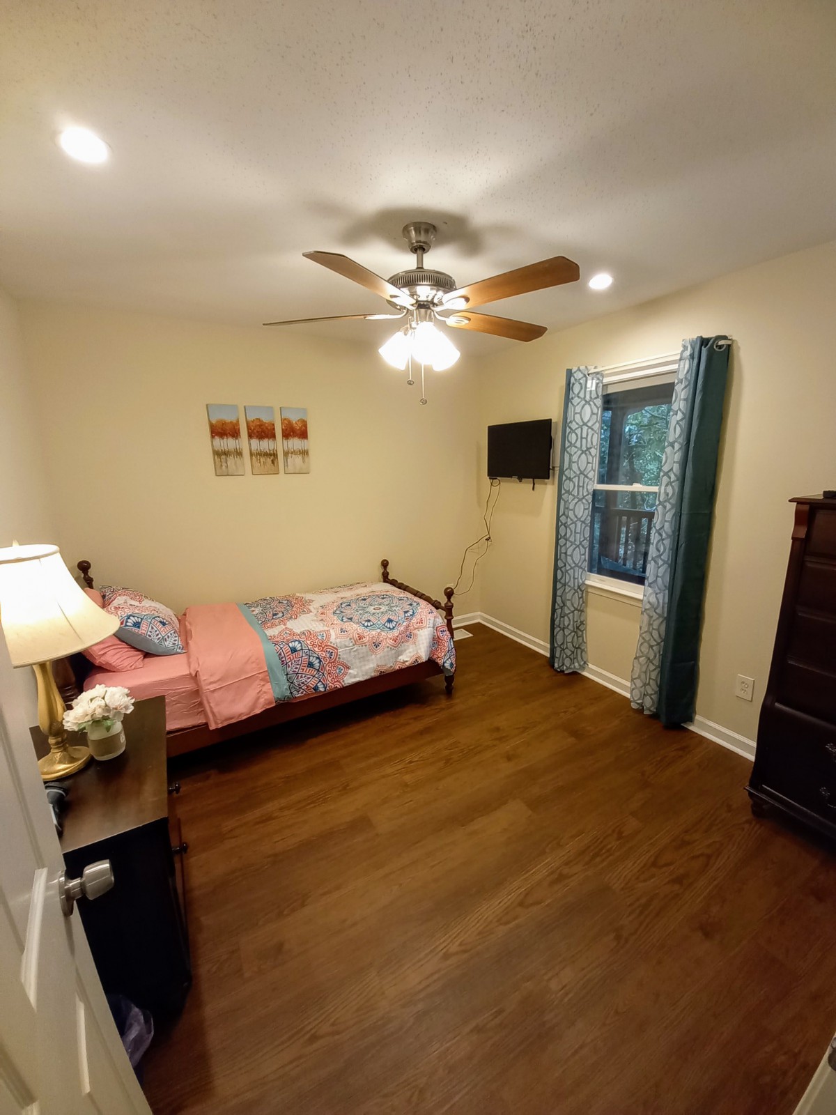 A cozy bedroom with a single bed, ceiling fan, and wooden flooring.