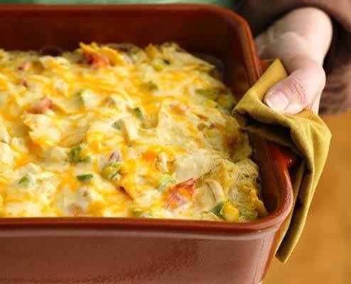 A freshly baked casserole with melted cheese and vegetables, being handled with an oven mitt.