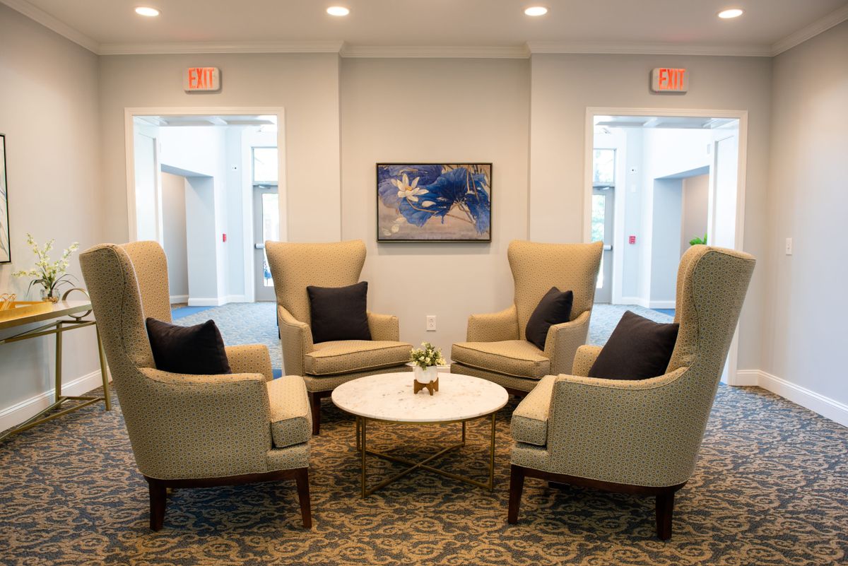 A cozy lobby seating area with four high-backed armchairs surrounding a round coffee table, adorned with decorative pillows and modern artwork on the wall.