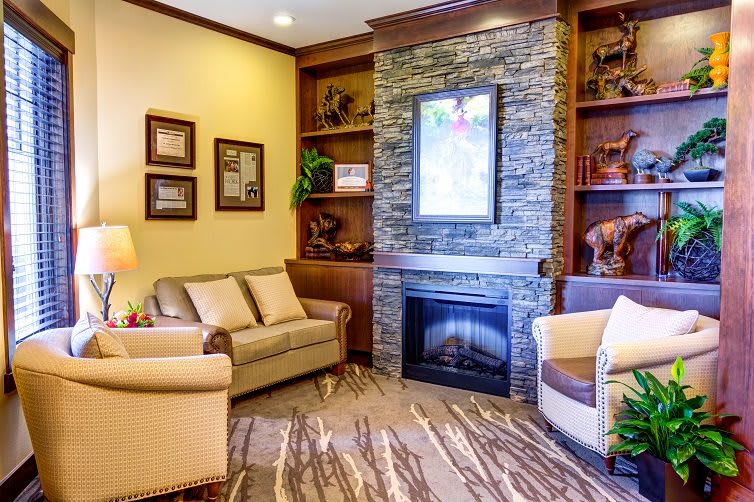 A cozy living room with a stone fireplace, comfortable seating, and decorative shelves.