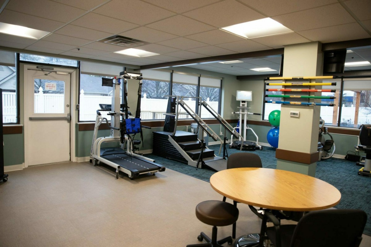 A physical therapy room equipped with various rehabilitation equipment, including a treadmill and parallel bars.