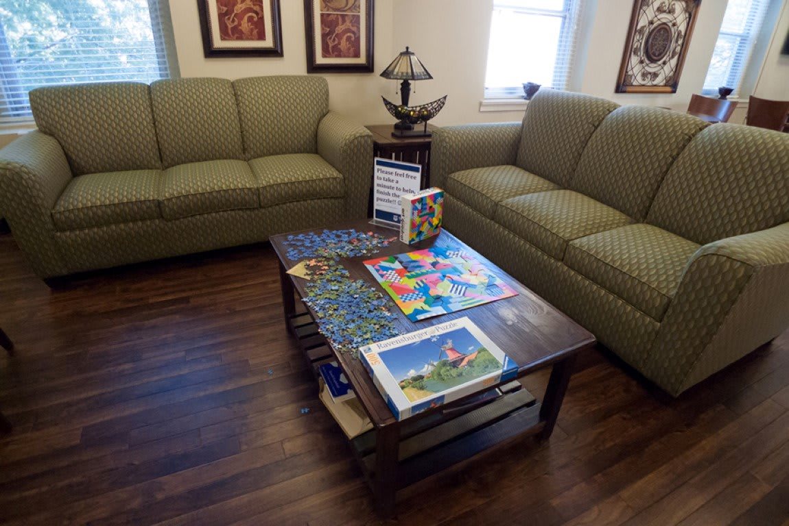 A cozy living room with two sofas, a coffee table featuring puzzles, and decorative artwork on the walls.