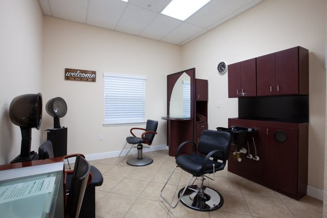 A well-organized hair salon room with chairs, a mirror, and cabinets.
