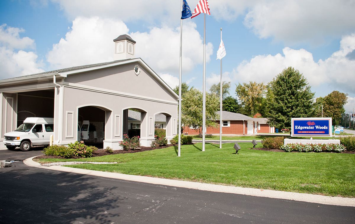 A building with three flag poles surrounded by a lawn and trees under a partly cloudy sky.
