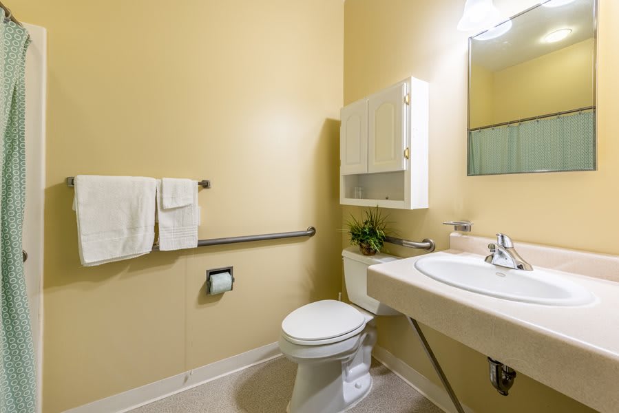 A clean and modern bathroom featuring a toilet, sink, mirror, and wall cabinet.