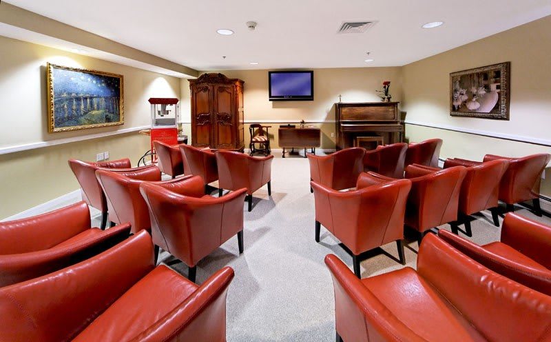 A cozy home theater room with red chairs, a television, piano, and popcorn machine.
