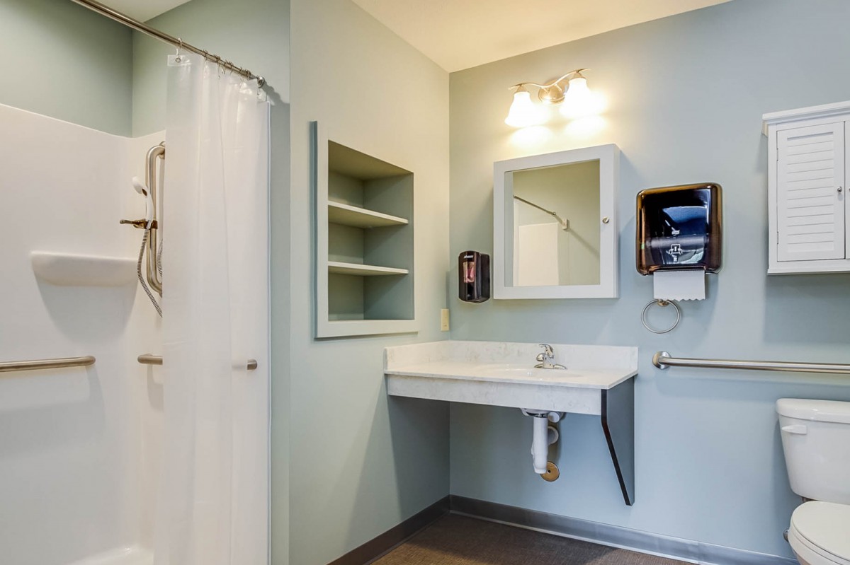 A modern accessible bathroom with a wall-mounted sink, mirror, and shower curtain.
