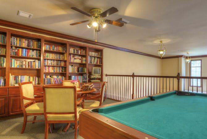 A cozy game room featuring a billiards table and a library area with bookshelves and a seating arrangement.